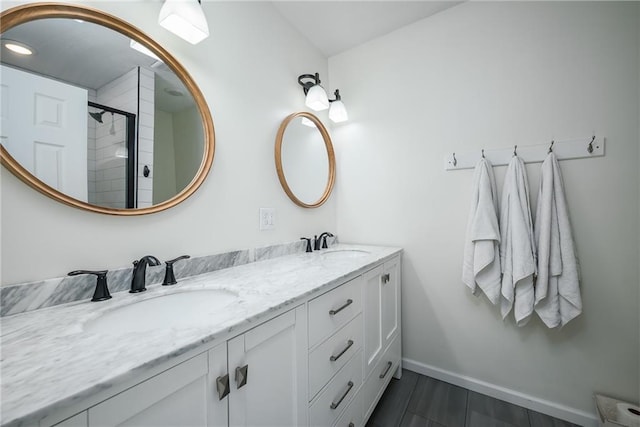 bathroom with double vanity, a sink, baseboards, and a tile shower