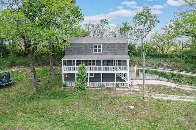 rear view of property with covered porch, roof with shingles, a trampoline, a lawn, and stairs