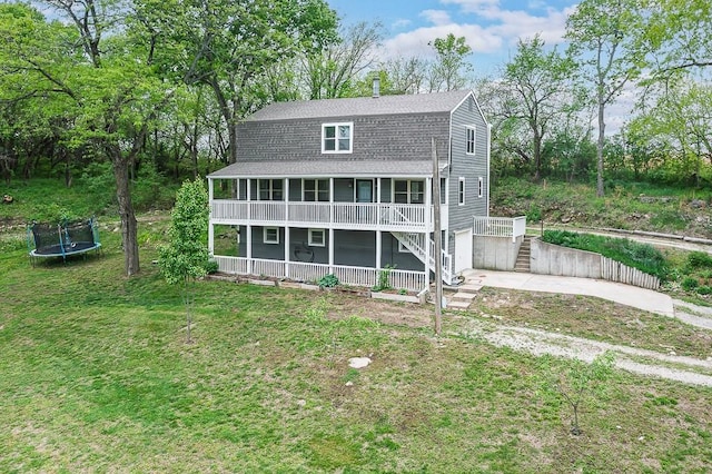 rear view of house featuring driveway, a trampoline, a yard, a shingled roof, and stairs