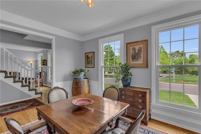 dining space featuring crown molding, wainscoting, a textured ceiling, light wood-style flooring, and stairs