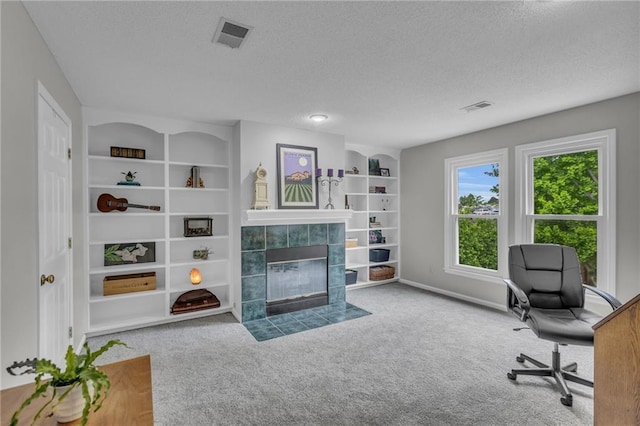 carpeted home office featuring a textured ceiling, visible vents, a tiled fireplace, and built in features