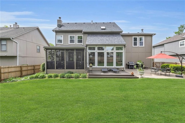 back of property with fence, roof with shingles, a sunroom, a patio area, and a yard