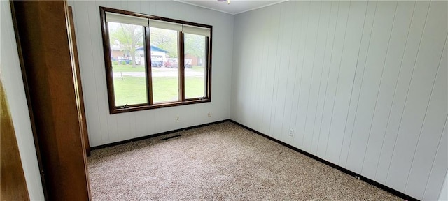 1620 Neosho St, Humboldt, KS 66748 - carpeted empty room with baseboards, visible vents, wooden walls, and crown molding