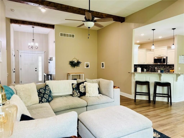 living room featuring visible vents, beamed ceiling, ceiling fan with notable chandelier, and light wood-style floors