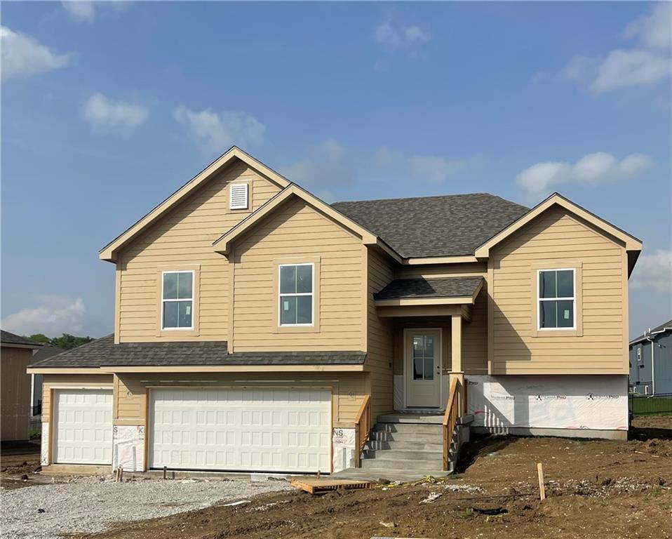 split foyer home with driveway, a garage, and roof with shingles