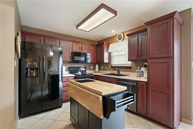 kitchen with a kitchen island, a sink, light tile patterned floors, black appliances, and butcher block counters