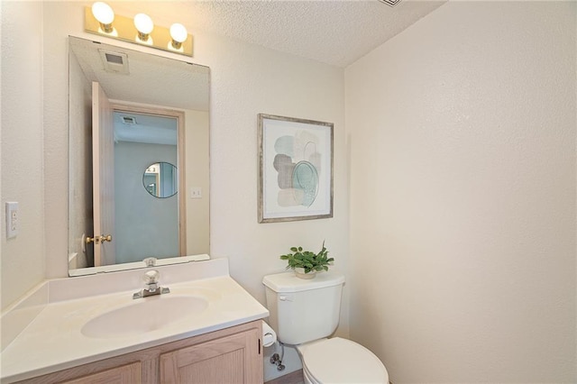 bathroom with vanity, toilet, a textured ceiling, and visible vents