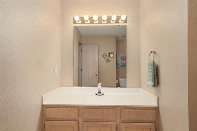 bathroom featuring vanity, a textured wall, and toilet