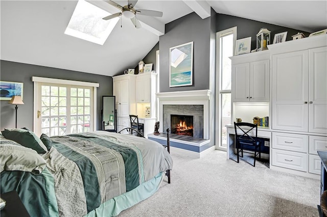 bedroom with a ceiling fan, a lit fireplace, light carpet, and vaulted ceiling with skylight