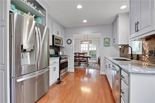 kitchen with appliances with stainless steel finishes, tasteful backsplash, a sink, recessed lighting, and light wood-style flooring