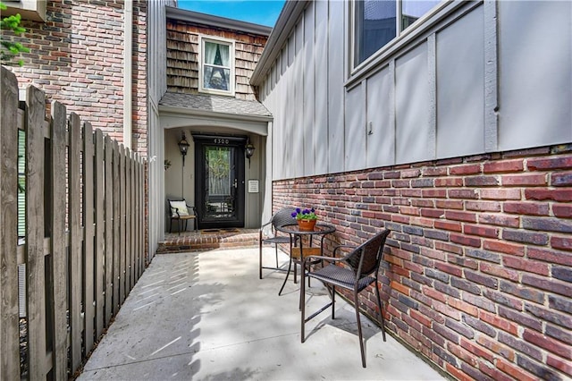 property entrance featuring board and batten siding, brick siding, fence, and a patio area