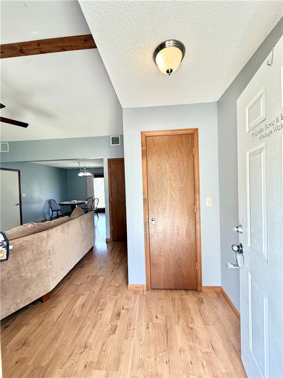 foyer entrance with baseboards, light wood finished floors, a textured ceiling, and visible vents