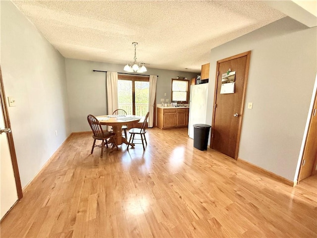 dining area with baseboards, light wood finished floors, a textured ceiling, and a chandelier