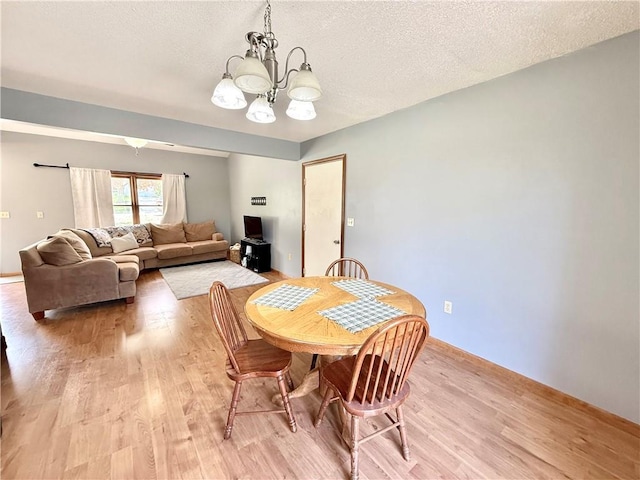 dining room with baseboards, light wood finished floors, a textured ceiling, and a chandelier