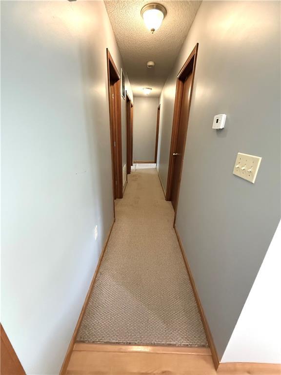 corridor with a textured ceiling, light carpet, and baseboards
