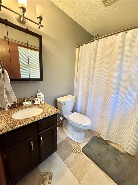 full bathroom with a shower with curtain, a textured ceiling, vanity, tile patterned floors, and toilet