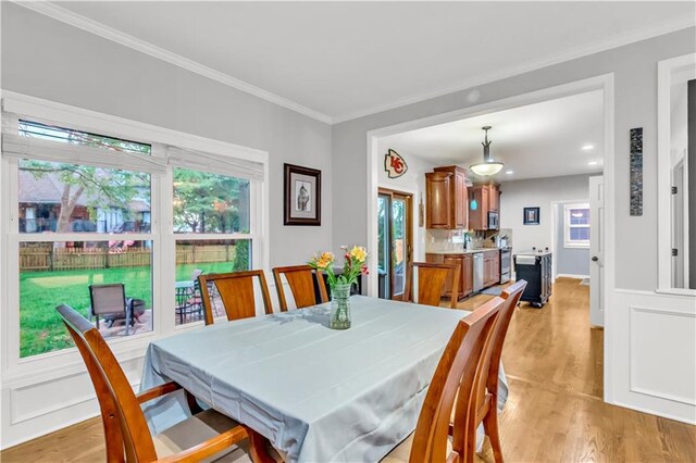dining area with light wood-style floors, crown molding, and a healthy amount of sunlight