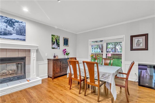 dining room with ornamental molding, a fireplace, wainscoting, and light wood-style flooring