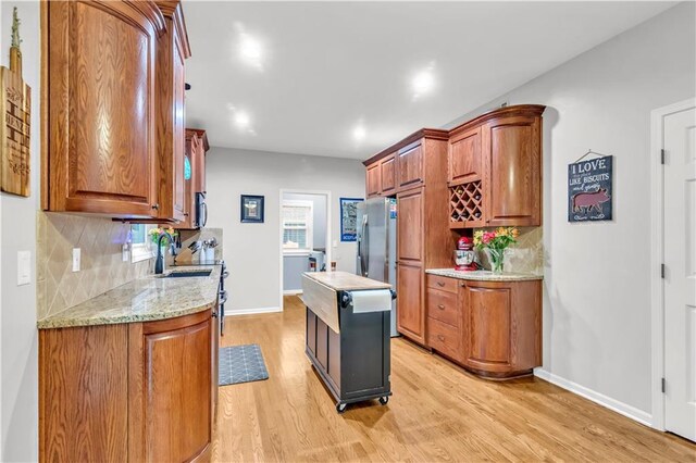 kitchen with light wood-type flooring, a sink, decorative backsplash, and brown cabinetry