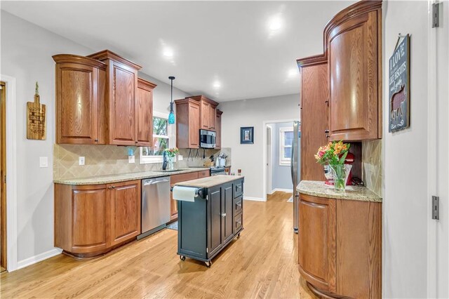 kitchen with appliances with stainless steel finishes, decorative backsplash, a sink, and light wood finished floors