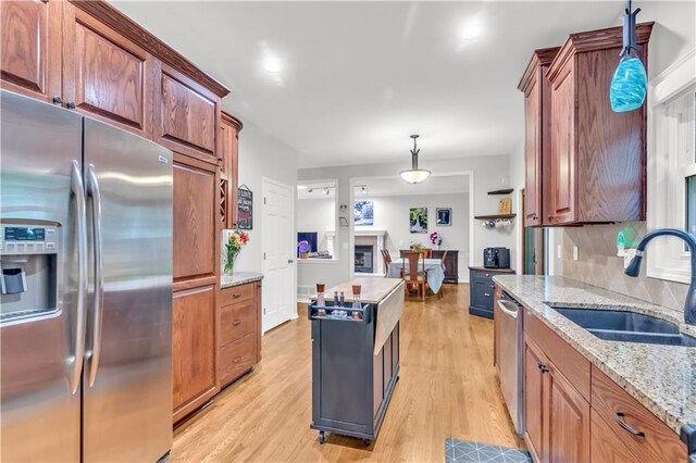 kitchen featuring a sink, light wood-style floors, stainless steel appliances, backsplash, and pendant lighting