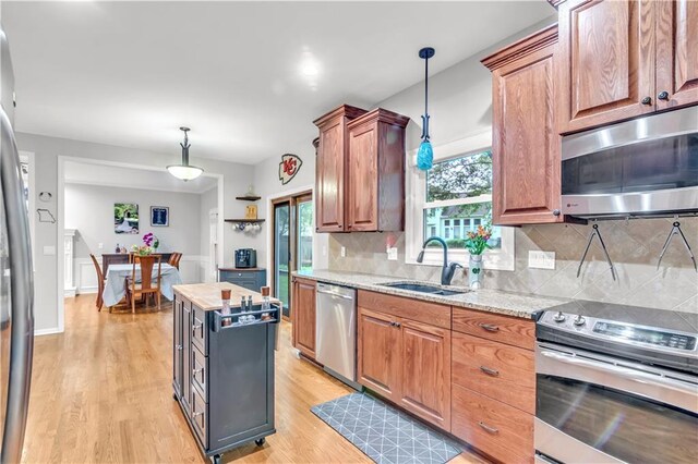 kitchen with tasteful backsplash, a sink, light stone counters, stainless steel appliances, and light wood-style flooring