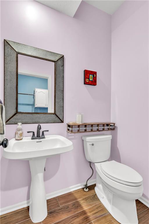 half bathroom with baseboards, a sink, wood finished floors, and toilet