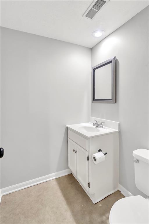 half bath featuring vanity, baseboards, toilet, and visible vents