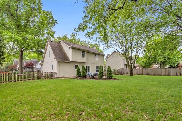 rear view of house with a lawn, a shingled roof, and a fenced backyard
