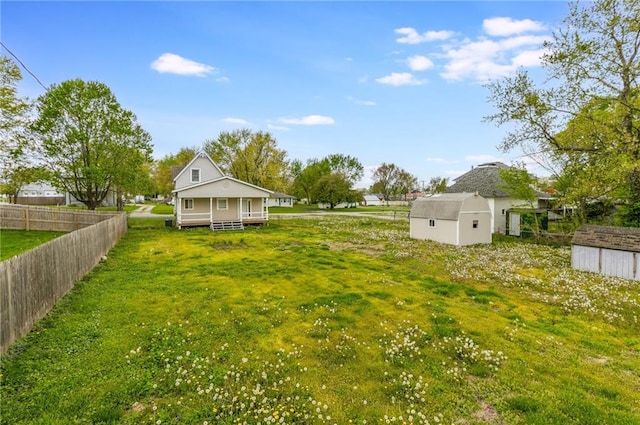 view of yard featuring covered porch, fence, an outbuilding, and a shed