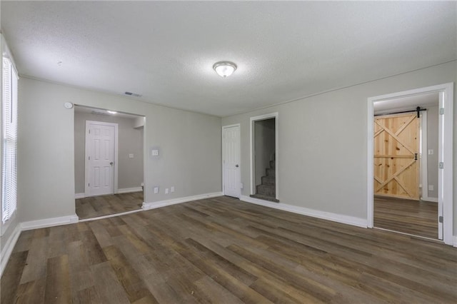 unfurnished room with a textured ceiling, a barn door, wood finished floors, baseboards, and stairs