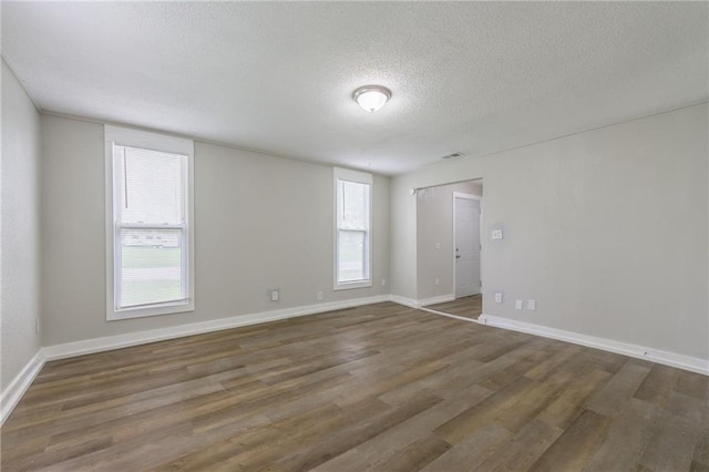 unfurnished room featuring baseboards, a textured ceiling, wood finished floors, and visible vents