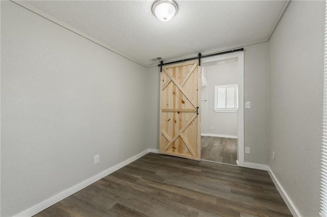 empty room featuring a textured ceiling, visible vents, a barn door, baseboards, and dark wood-type flooring