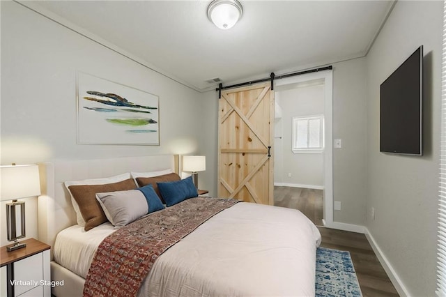 bedroom with baseboards, a barn door, wood finished floors, and visible vents