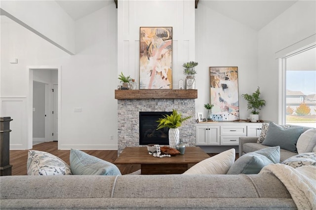 living room featuring baseboards, high vaulted ceiling, a stone fireplace, and wood finished floors
