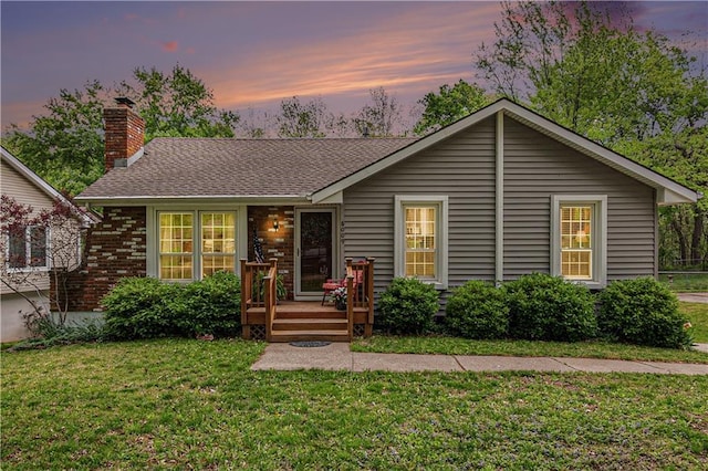 ranch-style home with a wooden deck, a chimney, brick siding, a shingled roof, and a lawn