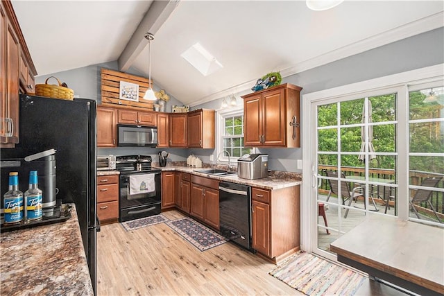 kitchen with brown cabinets, a sink, black appliances, light wood finished floors, and lofted ceiling with skylight