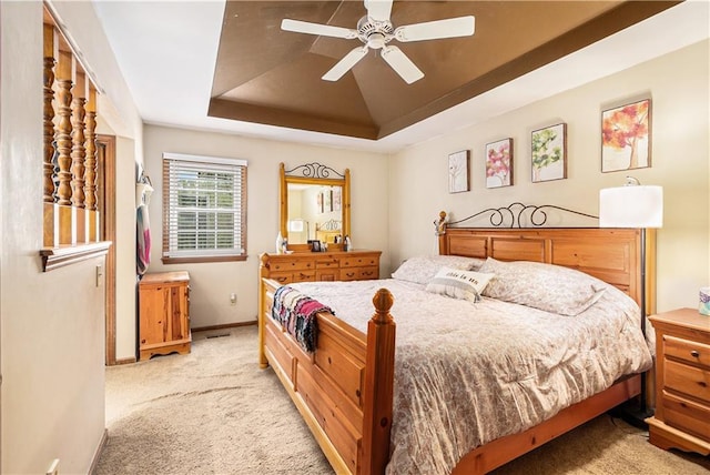 bedroom featuring light colored carpet, a ceiling fan, baseboards, and a tray ceiling