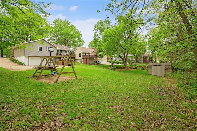 view of yard featuring a storage unit, an attached garage, a deck, an outbuilding, and concrete driveway