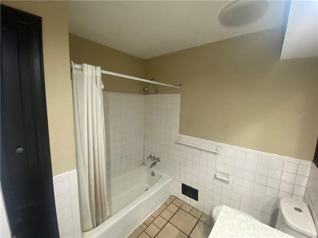 bathroom featuring a wainscoted wall, shower / bath combo with shower curtain, toilet, tile walls, and tile patterned floors