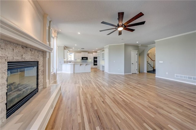 24108 W 67th Ter, Shawnee, KS 66226 - unfurnished living room with a fireplace, ornamental molding, a ceiling fan, stairway, and light wood-style floors