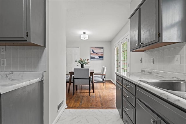 kitchen featuring baseboards, marble finish floor, backsplash, and gray cabinetry