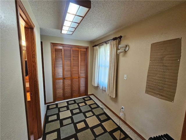 doorway with tile patterned floors, a textured ceiling, a textured wall, and baseboards