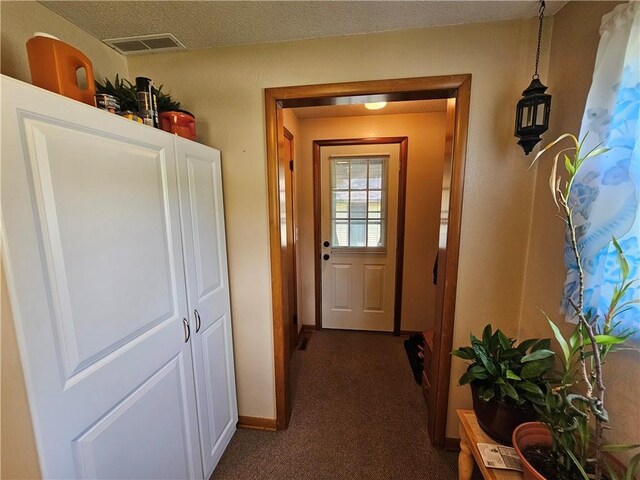 doorway to outside with a textured ceiling, visible vents, dark colored carpet, and baseboards
