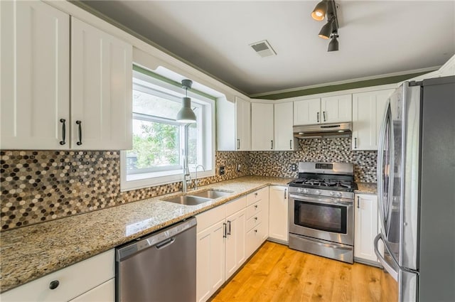 kitchen with appliances with stainless steel finishes, light wood-type flooring, a sink, under cabinet range hood, and white cabinetry