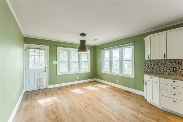 unfurnished dining area featuring baseboards, visible vents, ornamental molding, and light wood-type flooring