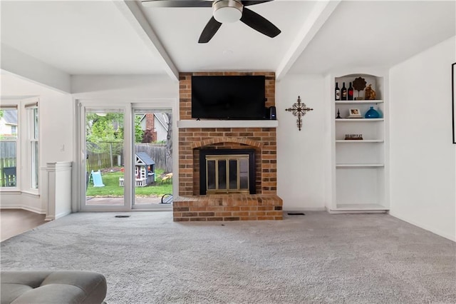 living area featuring a ceiling fan, carpet, a brick fireplace, and beam ceiling