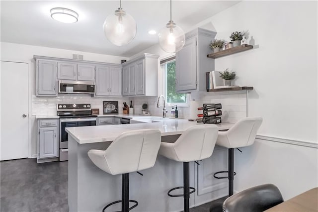 kitchen with a peninsula, backsplash, gray cabinetry, and stainless steel appliances