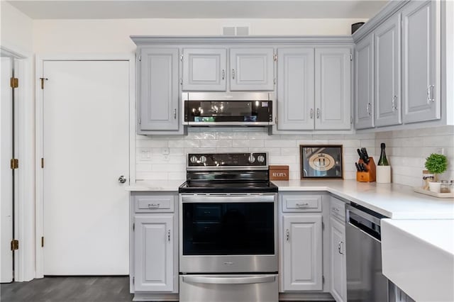 kitchen with light countertops, decorative backsplash, gray cabinetry, and stainless steel appliances
