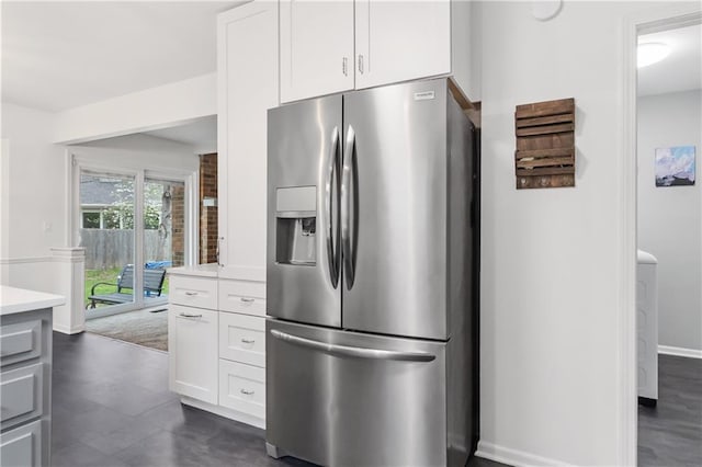 kitchen with baseboards, stainless steel fridge, light countertops, white cabinetry, and dark tile patterned flooring
